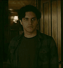 a man in a black shirt and plaid jacket is standing in a dark room .