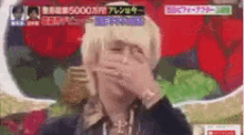 a man with blonde hair is covering his mouth with his hands .
