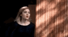 a woman in a black dress is standing in front of a curtain .