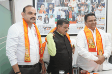 three men are standing in front of a wall with a picture of a man with a mustache