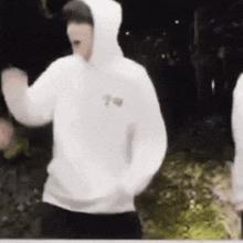 a man in a white hoodie is dancing in front of a crowd .