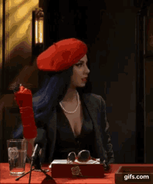 a woman wearing a red beret is sitting at a table with a microphone and a box that says fuck no