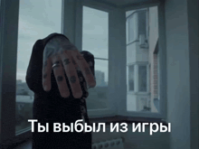 a man with a ring on his finger is standing in front of a window with russian writing on it