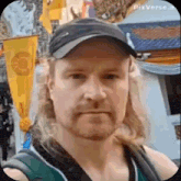 a man with long blonde hair and a beard is wearing a hat and taking a selfie .