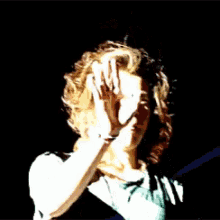 a man with long hair and a green shirt is standing in the dark