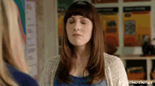 a woman is standing in a classroom with her eyes closed .