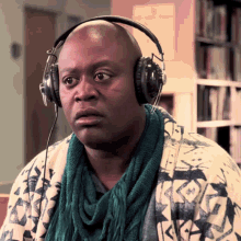 a bald man wearing headphones and a green scarf looks at the camera