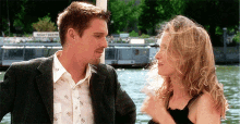 a man and woman are looking at each other in front of a body of water