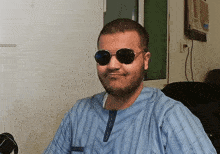 a man wearing sunglasses and a blue shirt smiles for the camera