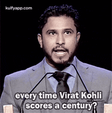 a man in a suit and tie is standing in front of a microphone and talking about virat kohli .