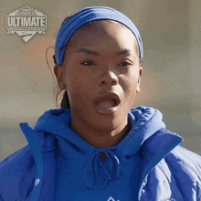 a woman wearing a headband and a blue jacket is standing in front of a sign that says ultimate challenge
