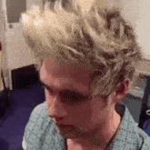 a young man with blonde hair is sitting in a room with his eyes closed .