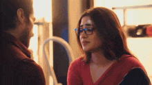 a man and a woman are looking into each other 's eyes . the woman is wearing glasses and a red shirt .