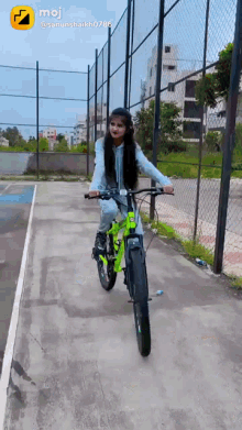 a girl is riding a green bicycle on a road with a moji icon on the bottom right