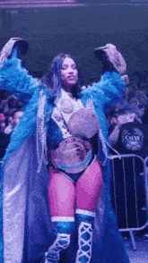 a woman in a blue coat is holding two championship belts in her hands .