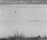 a black and white photo of a helicopter flying over a body of water