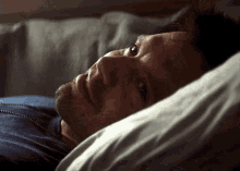 a man with a beard is laying in a bed with his head on a pillow