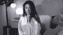 a black and white photo of a woman sitting on a bed in a bedroom .