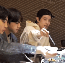 a group of young men are sitting at a table with chopsticks in their hands .