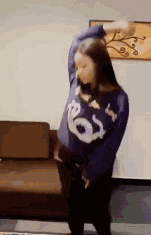a woman in a purple sweater is dancing in front of a couch .