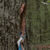a woman in a plaid shirt stands behind a tree