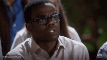 a man wearing glasses is making a funny face while sitting in a classroom .