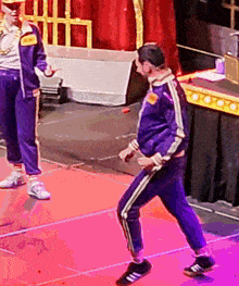 a man in a purple tracksuit is dancing on a stage with a man in a gold chain