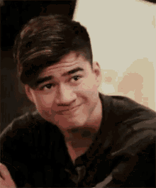 a young man in a black shirt is making a funny face and smiling .
