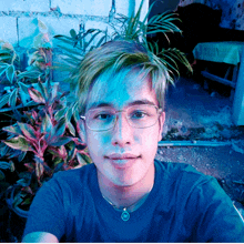 a man wearing glasses and a blue shirt has a pendant with the letter m on it