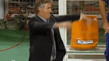 a man in a suit and tie is standing next to an orange seat