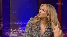 a woman in a plaid jacket is sitting in front of a television screen and making a funny face .