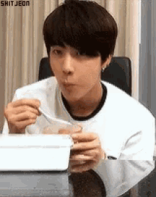 a young man is sitting at a table eating a meal with a spoon .