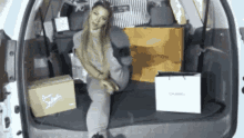 a woman is sitting in the trunk of a car surrounded by boxes and bags .