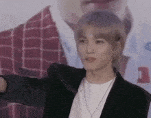a young man wearing a black jacket and a white shirt is standing in front of a poster .