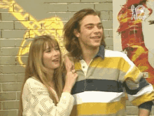 a man and a woman are standing next to each other in front of a brick wall .