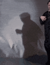 a shadow of a person is cast on a wall behind a man in a black shirt