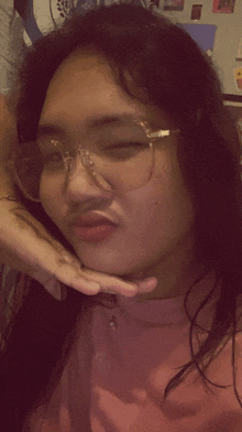 a woman wearing glasses and a pink shirt looks at the camera