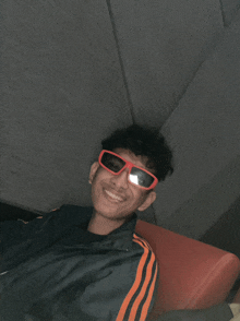 a young man wearing red sunglasses and an adidas jacket smiles