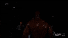 a man in a suit and tie is standing in front of a group of men and a sign that says aew live