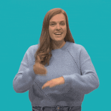 a woman wearing a blue sweater giving a thumbs up