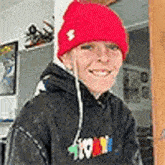 a young boy wearing a red knitted hat and a black hoodie is smiling .