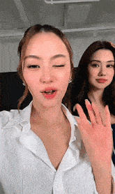 a woman in a white shirt winks at the camera while another woman waves her hand