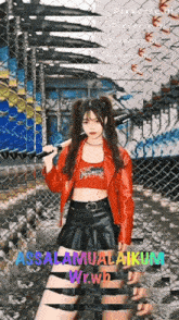 a girl in a red jacket and black skirt is holding a bat in front of a chain link fence that says assalamualaikum
