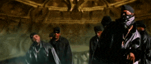 a group of men in black jackets and hats are standing in a dark room
