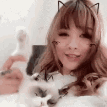 a woman with cat ears on her face is holding a cat in her arms .