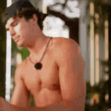 a shirtless man with a necklace around his neck is looking down at something .