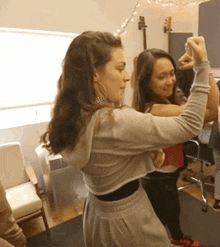 two women are dancing in a room with a guitar on the wall behind them