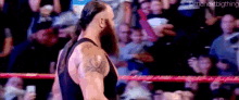 a man with a beard and tattoos is standing in a wrestling ring .