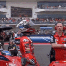 a motorcycle racer wearing a helmet is standing next to a red car on a race track .