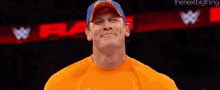 john cena is wearing an orange shirt and a blue hat while standing in front of a sign that says raw .